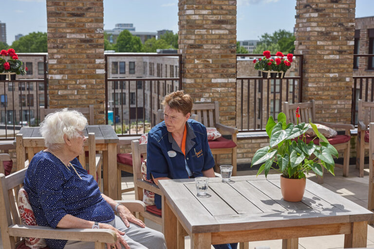 Verzorger samen met vrouw aan de tafel bij het gebouw kloosterkwartier GH